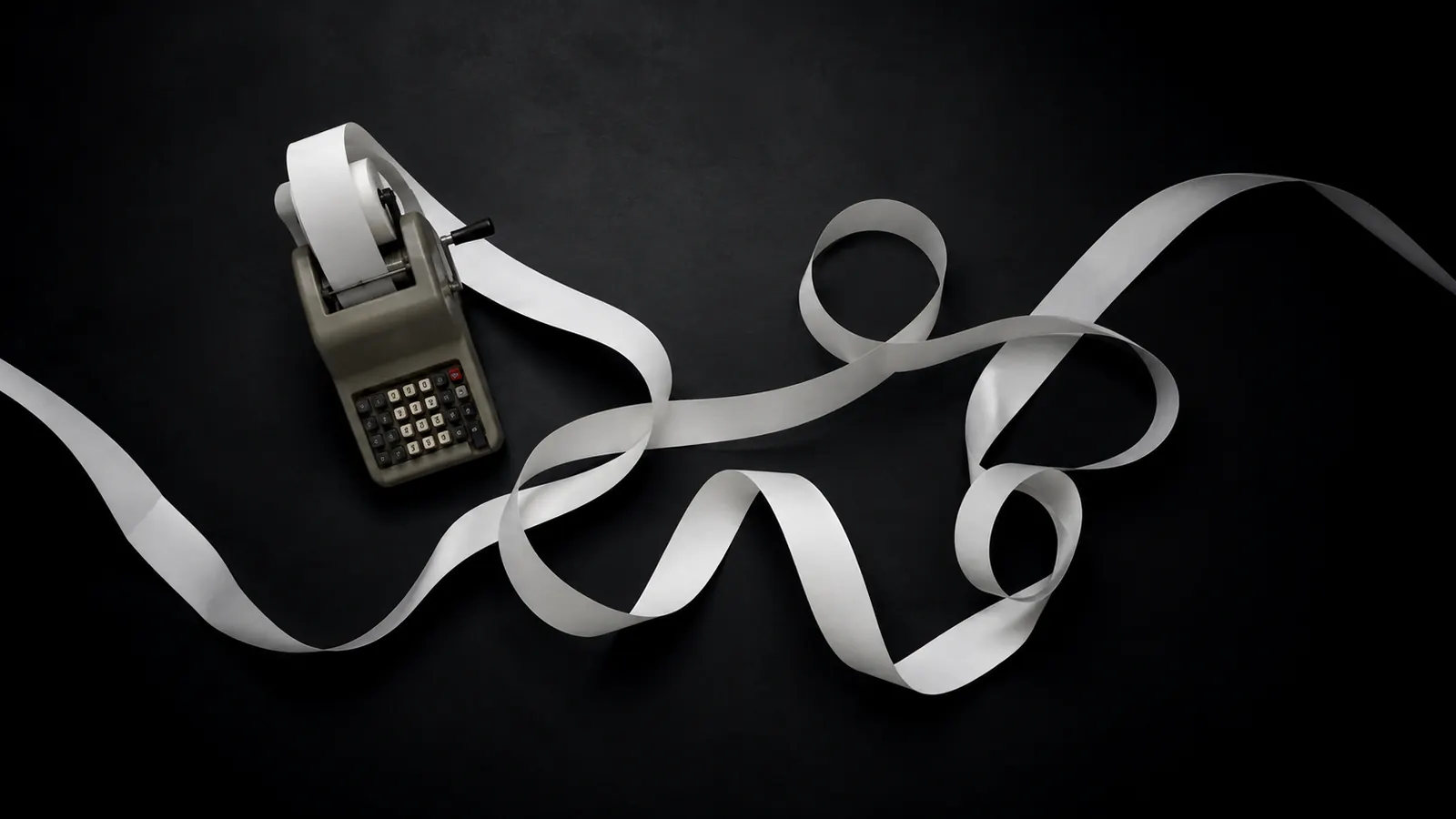 An adding-machine tape unspooling across a dark desk